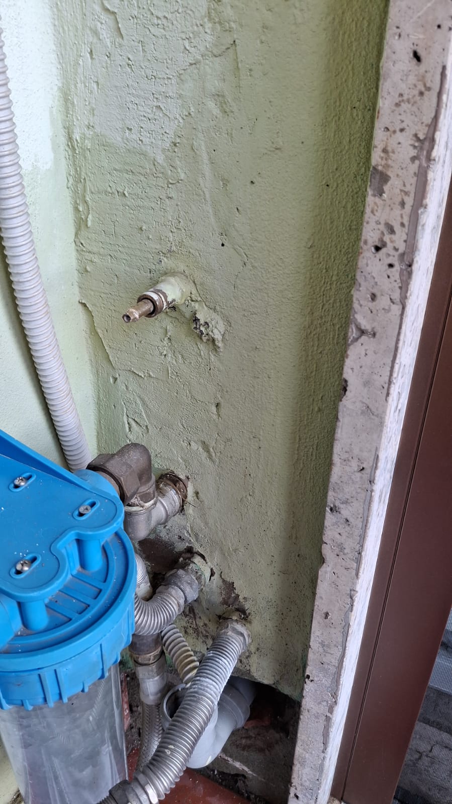 An exposed wall section shows plumbing connections, flexible hoses, and a blue cylindrical component.