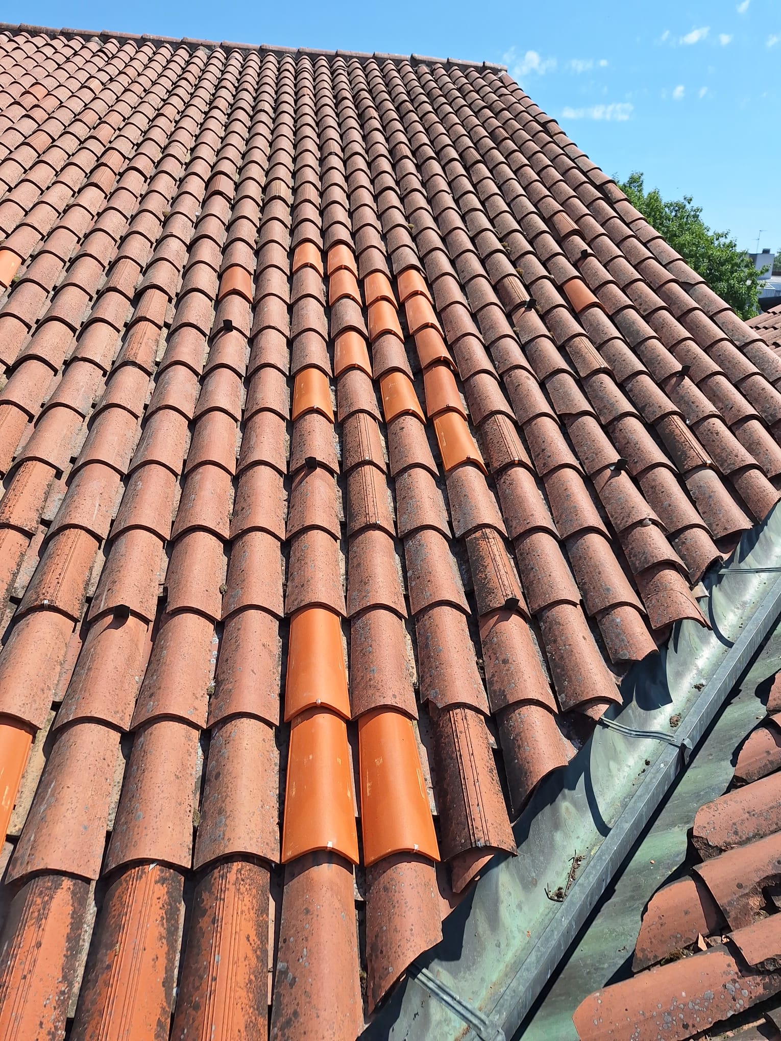 A broad tiled roof surface with rows of terracotta tiles is shown under a blue sky.